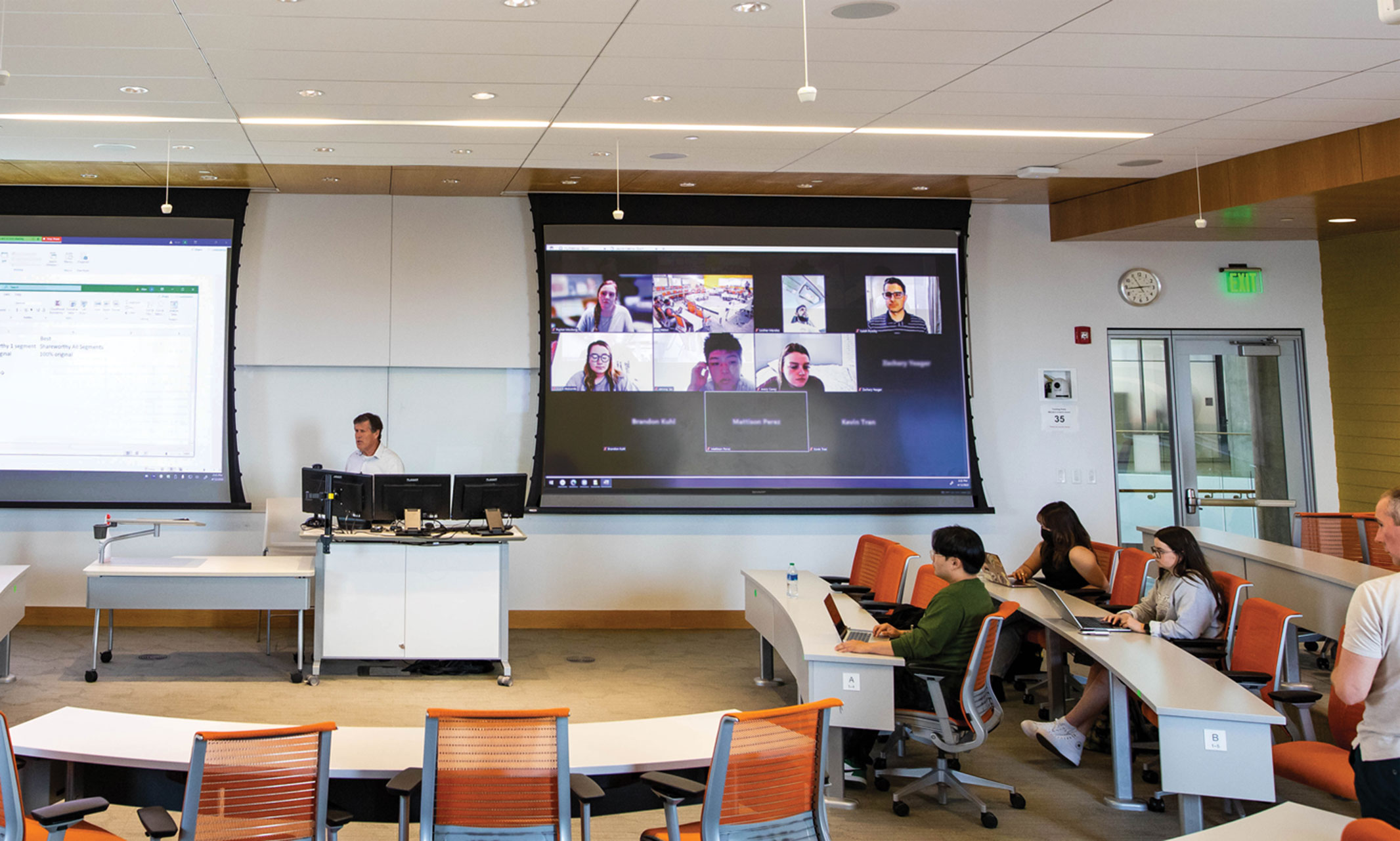 Students in a classroom, and students on a screen, listening to their professor