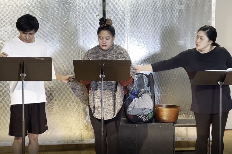 Three students stand in a row with stands in front of them, rehearsing lines for Bui's play