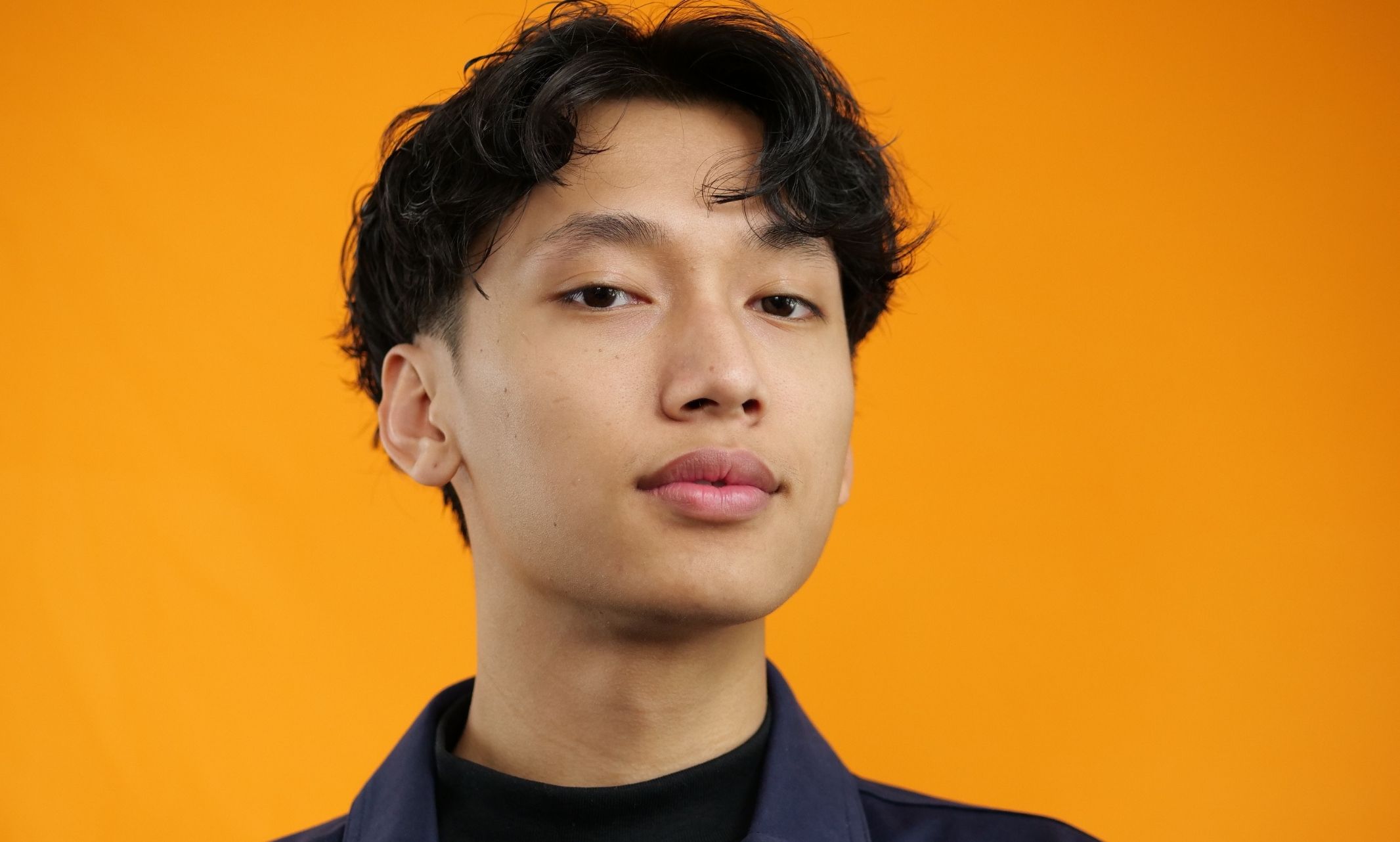 Hieu Bui from the shoulders up, standing in front of an orange background and looking at camera
