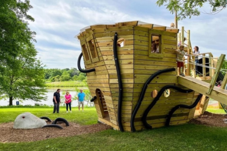 Children play in fort shaped like a pirate ship as parents watch in the background