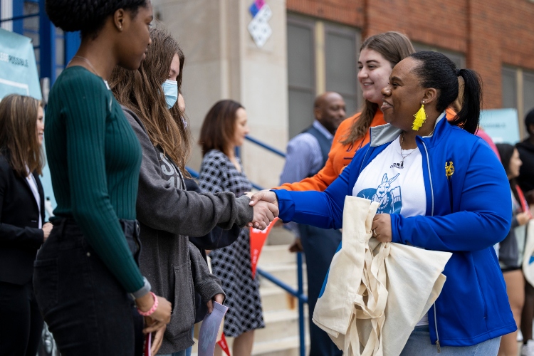 A woman in UMKC gear shakes hands with a student 