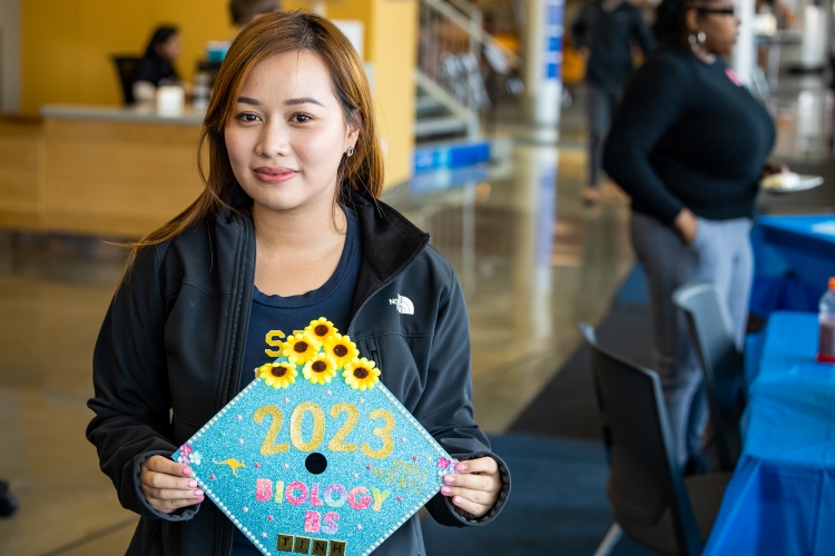 A first generation college student holds her graduation gap, which she has just decorated, inside the UMKC student union