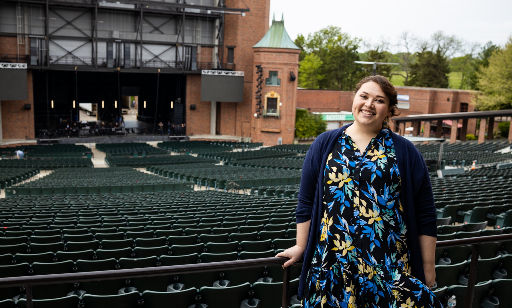 Roslinde Rivera stands smiling in the back of Starlight's seating area with rows of dark green chairs and the Starlight stage behind her.