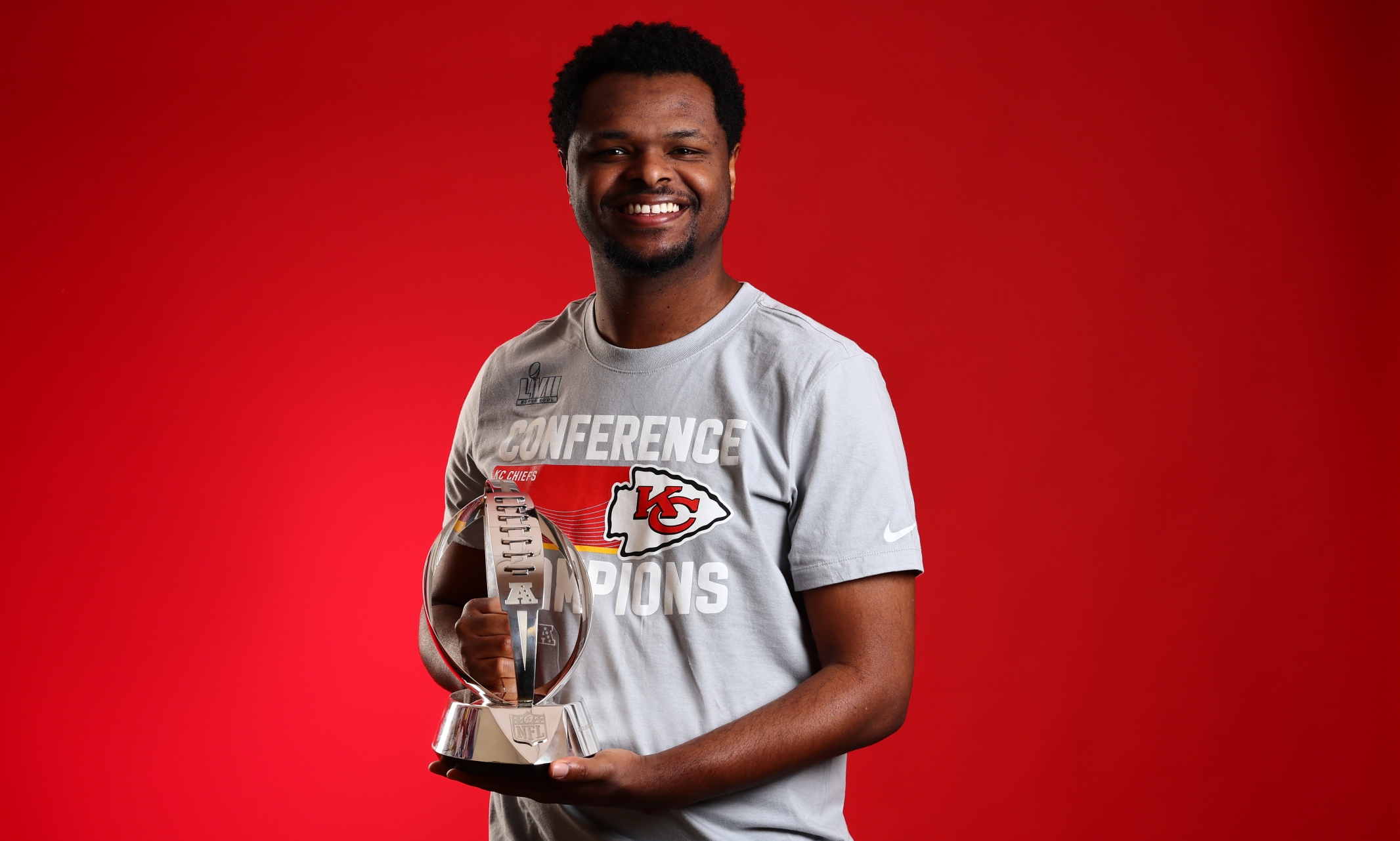 Ishmael Shumate holds the AFC Championship trophy smiling against a red backdrop