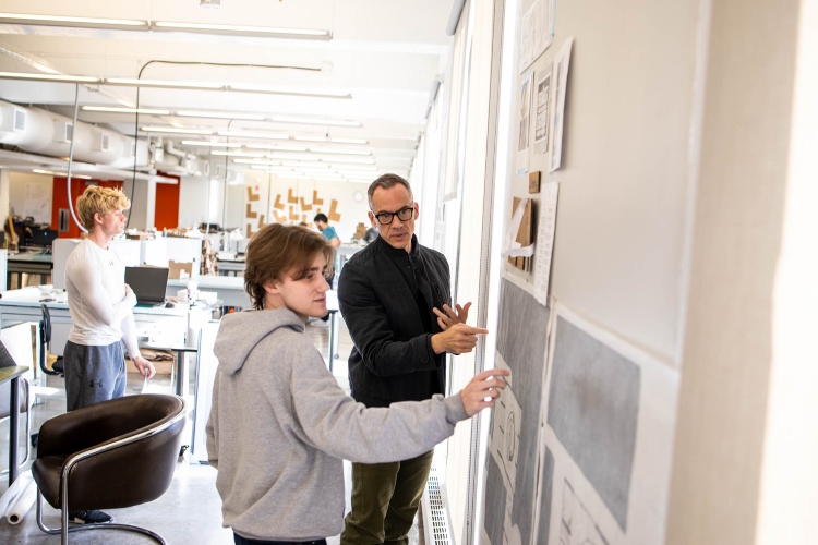 Isaiah and instructor John Eck look at drawings which are tacked up on the wall