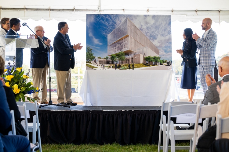 People stand on a podium. The rendering of the new health sciences sits in the middle with people on either side, applauding