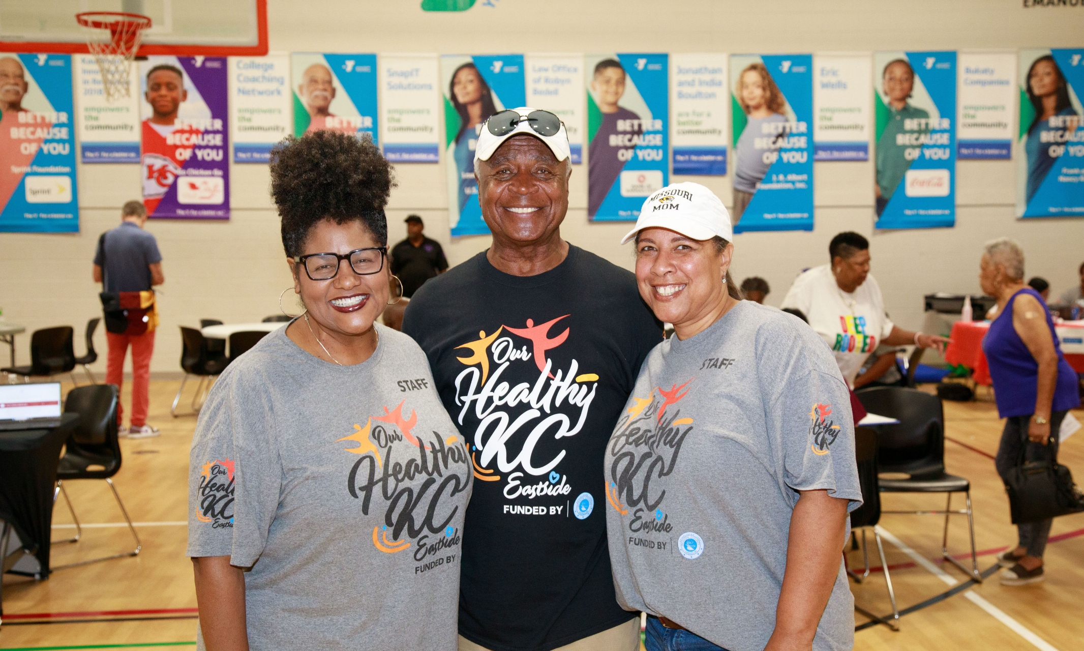 Three people stand in a gym with health-care screenings in background.