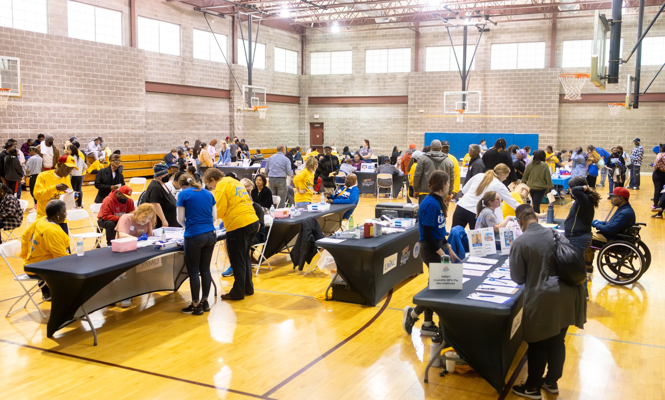 A gymnasium filled with people getting vaccinations, blood pressure checks and more while enjoying family entertainment