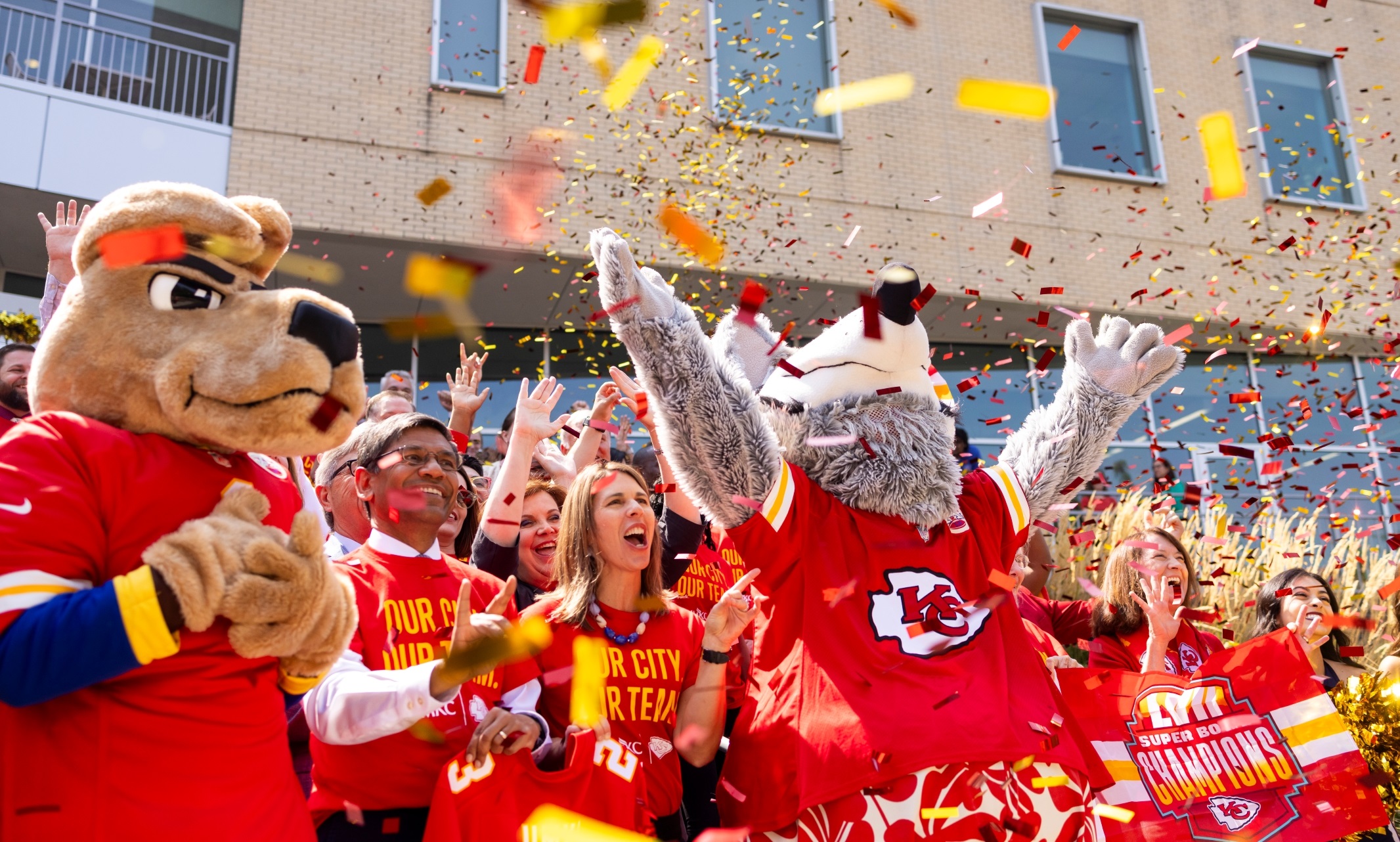 A large group of people, KC Wolf and KC Roo stand in front of the Student Union and cheer enthusiastically as red and gold confetti floats down onto them