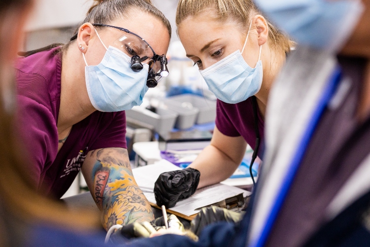 Two dental hygiene students look at something in the foreground of the photo together