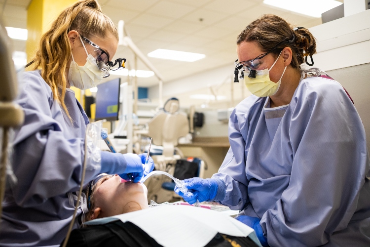 Two dental hygiene students clean a person's teeth in the UMKC dental clinic