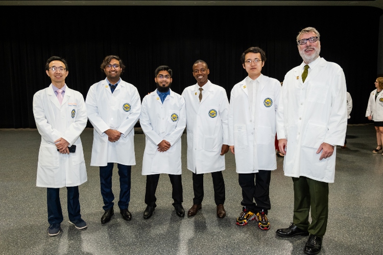 Pharmacy students stand smiling in white coats with faculty