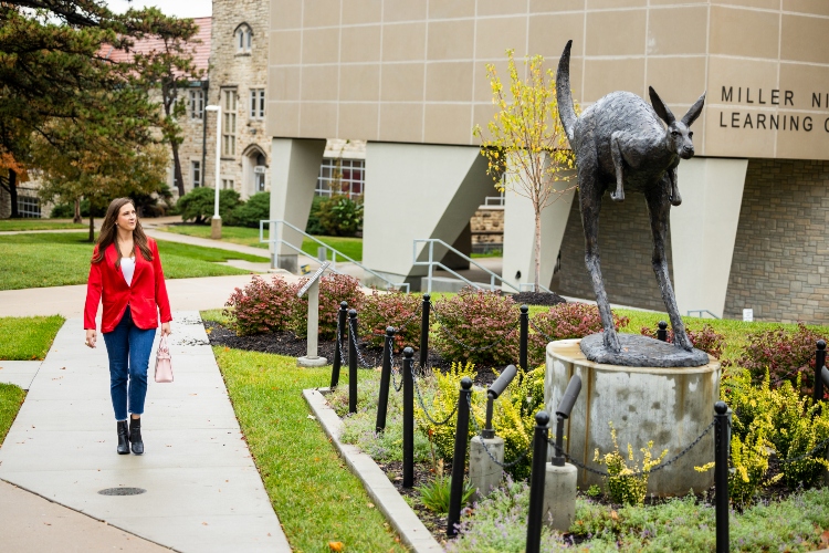 Meghan Jaben walks by the Corbin Roo statue on the UMKC Volker Campus wearing a bright red blazer