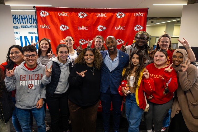 UMKC students spending time with Kansas City Chiefs Ramzee Robinson and Rooing Up in front of the UMKC and Chiefs back drop 