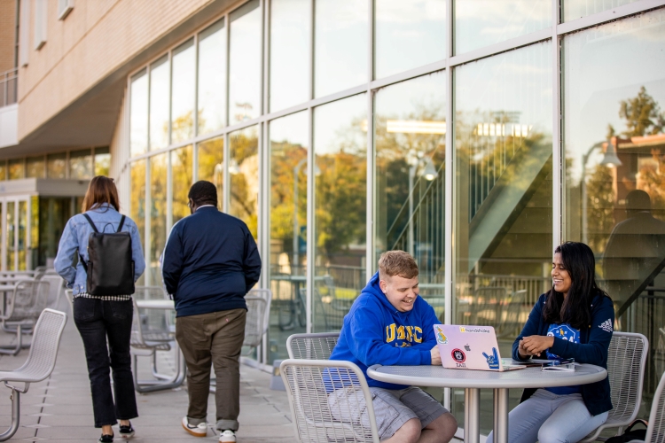 Two students sit outside on the Student Union rooftop studying.
