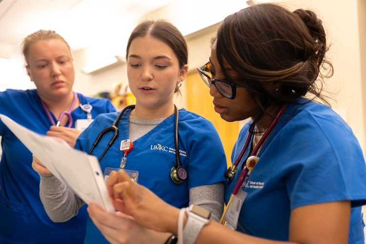 Tatyana Charles stands with two other nursing students discussing a simulation case and referring to a document