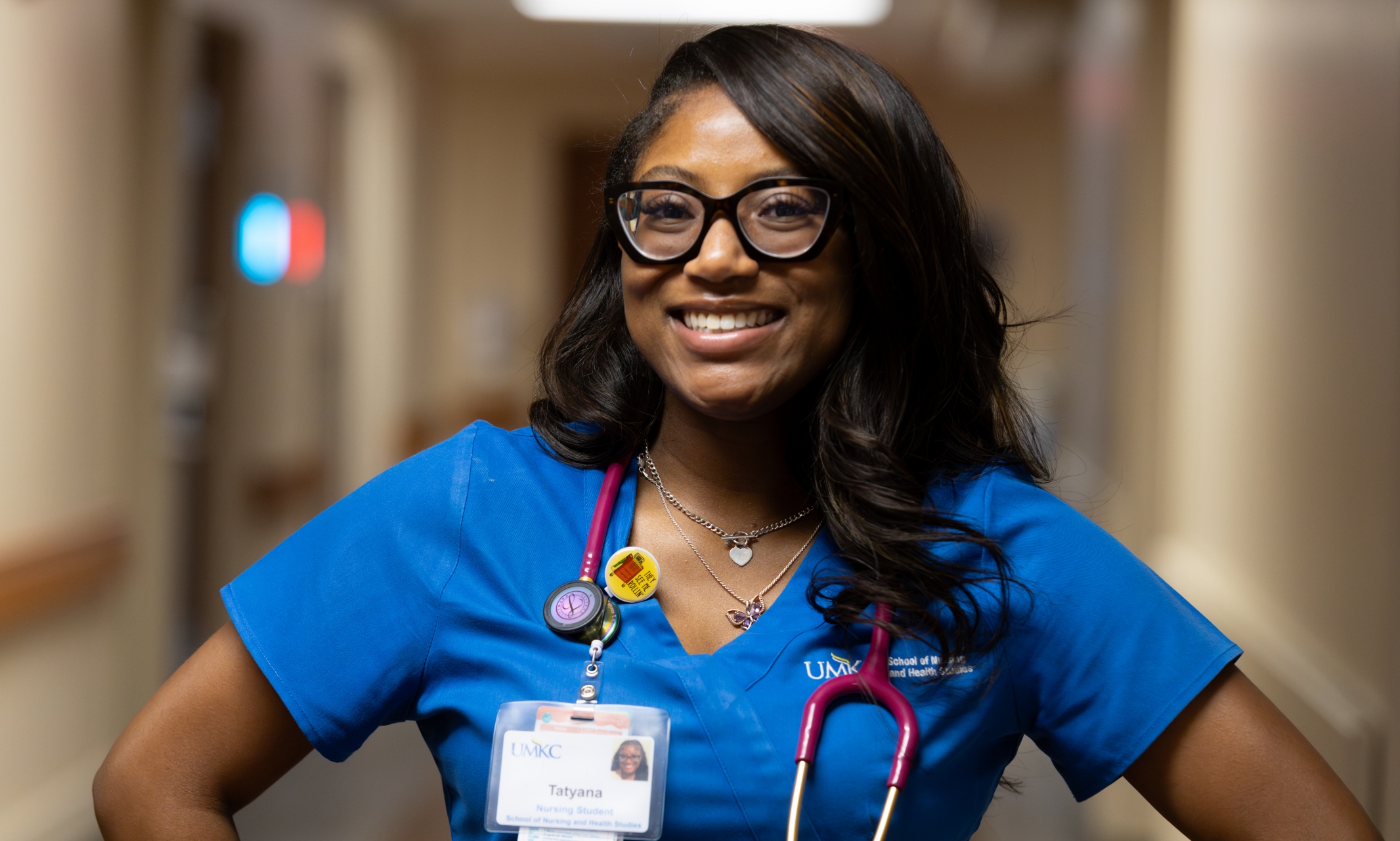 Tatyana Charles stands confidently, smiling in blue scrubs in the hall at University Health