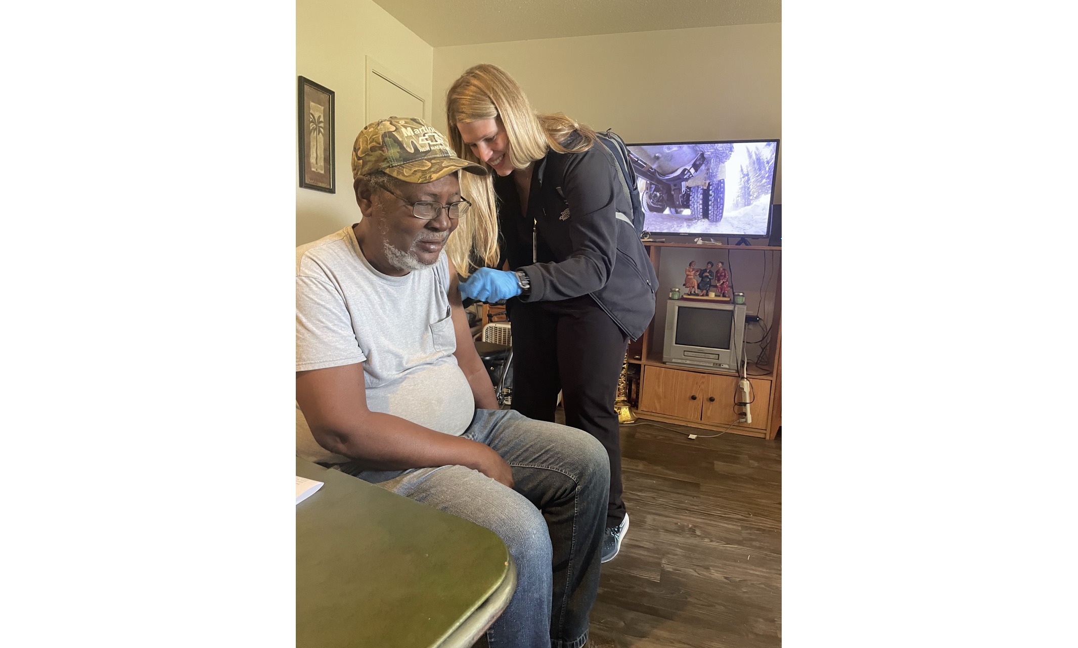 Blonde woman smiling while administering vaccination to middle-aged man in his home