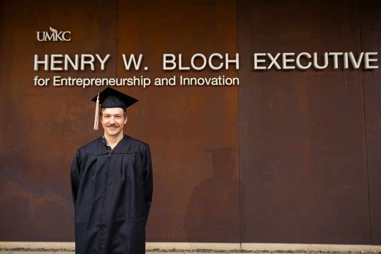 Cody Truitt wearing graduation regalia in front of Bloch Eexecutive Hall.