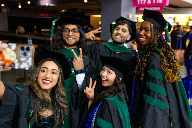Five graduates from School of Medicine pose for a selfie wearing their regalia
