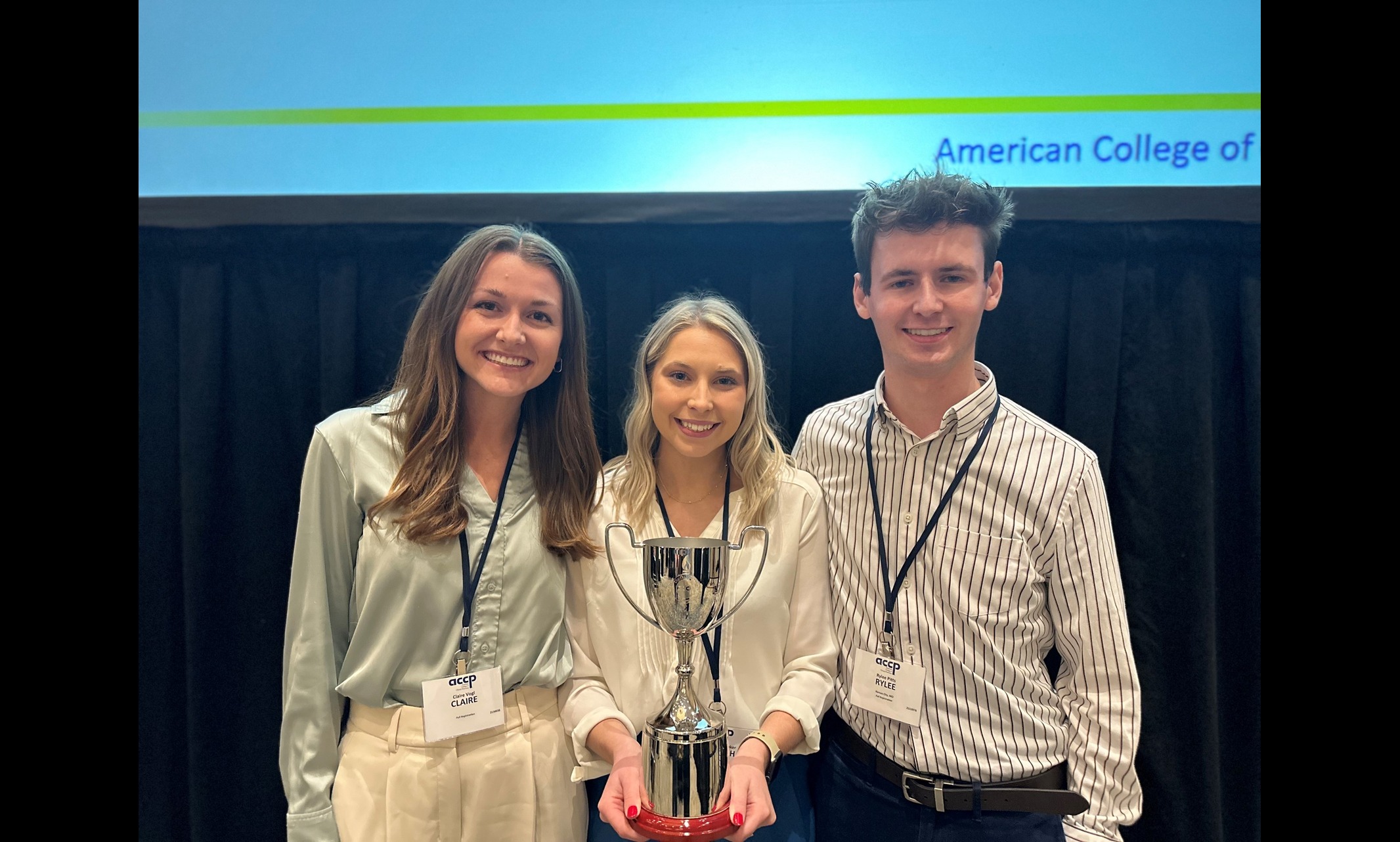 Three students standing with a trophy after winning competition