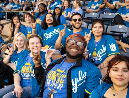 Group fronted by the chancellor and the KC Roo holding Kansas City Royals banner and holding up Roo sign with fingers