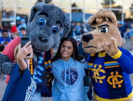 UMKC's kangaroo mascot and Sporting KC's dog mascot post with person wearing Sporting KC gear.