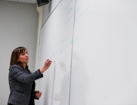 A professor writing on the whiteboard in front of her class. 