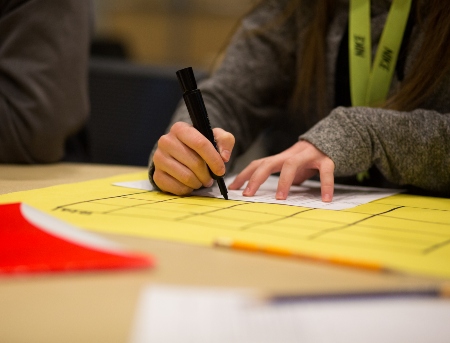 A student writing at their desk using a black marker. 