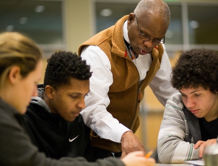 A professor helping students with an assignment as they sit at a round table in the classroom.