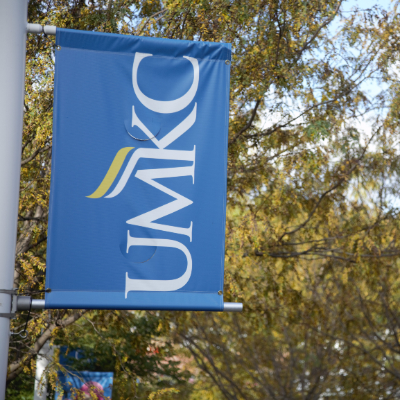A UMKC banner hanging on a light pole along a campus walking path.