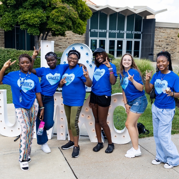 A group of students standing outside of the Atterbury Student Success center smiling and giving the roo-up hand sign.