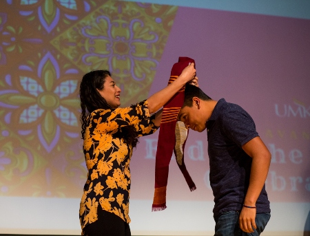 A faculty member and student stand on stage as the faculty member places and award sash over the shoulders of a student in the Avanzando program.
