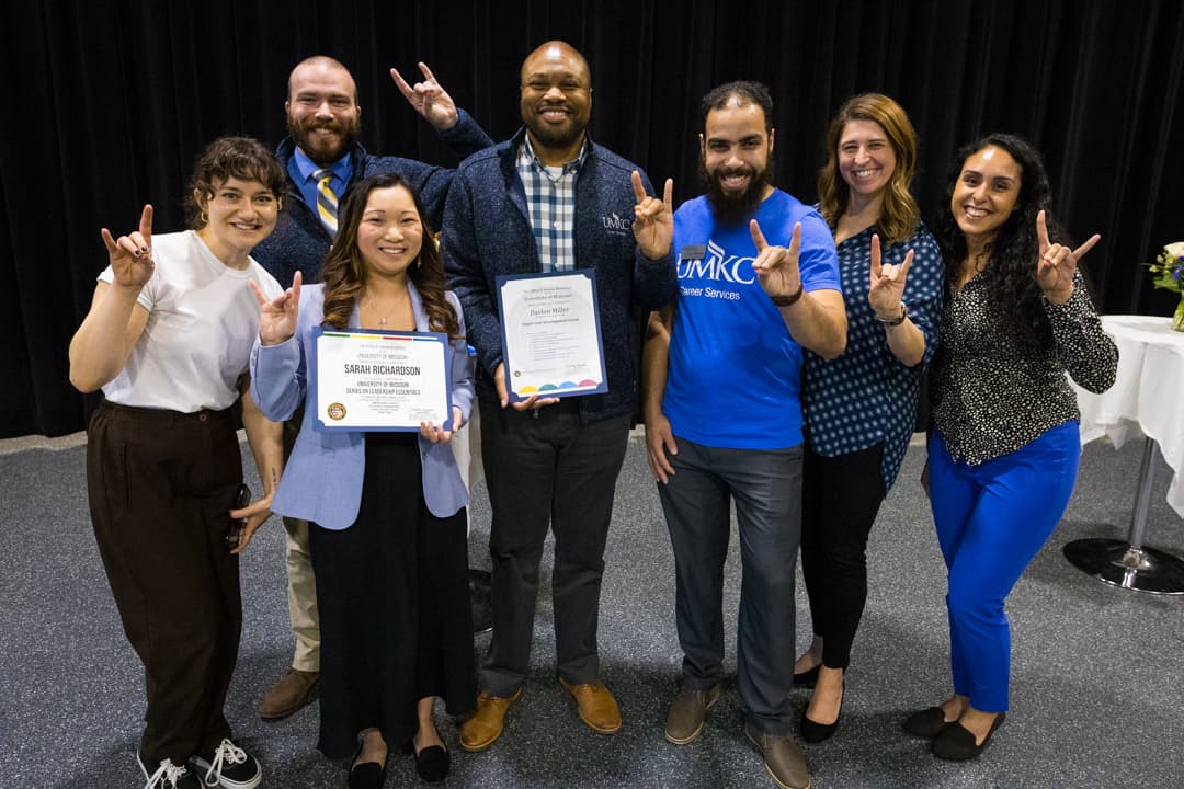 UMKC Career Services staff members look happy as they give the Roo Up hand sign and hold up a certificate of recognition at the staff awards.
