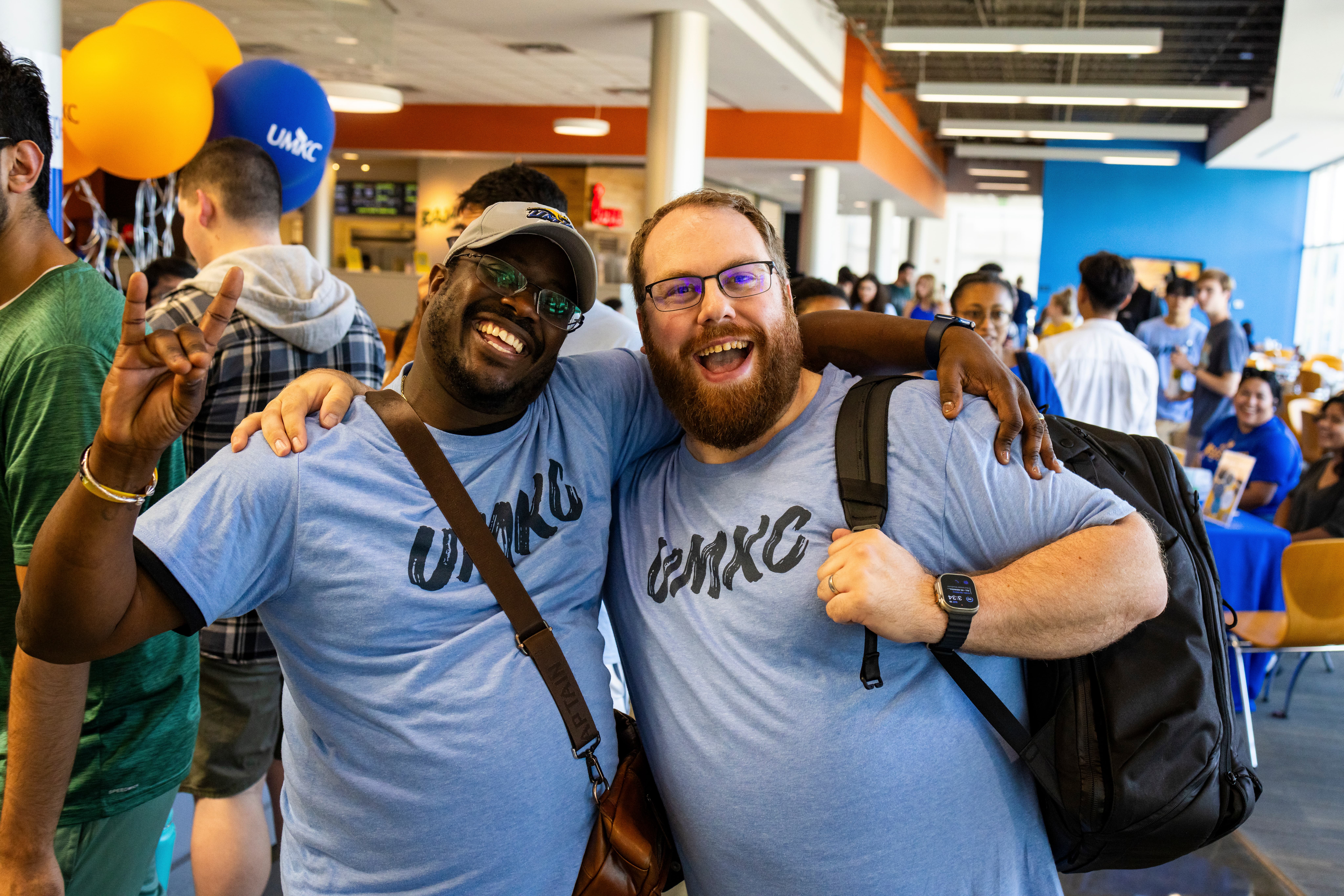 Two staff members looking happy have their arms around each other while wearing blue UMKC t-shirts during a soccer game