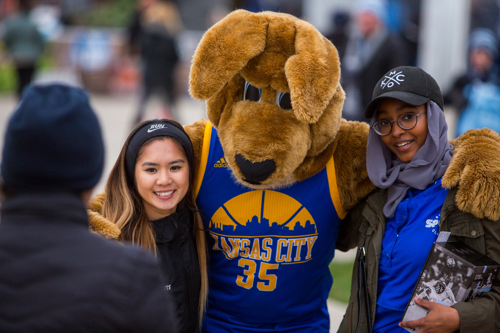 UMKC mascot Kasey Roo stands between two female students, one presenting as white and one wearing a hijab under her hat