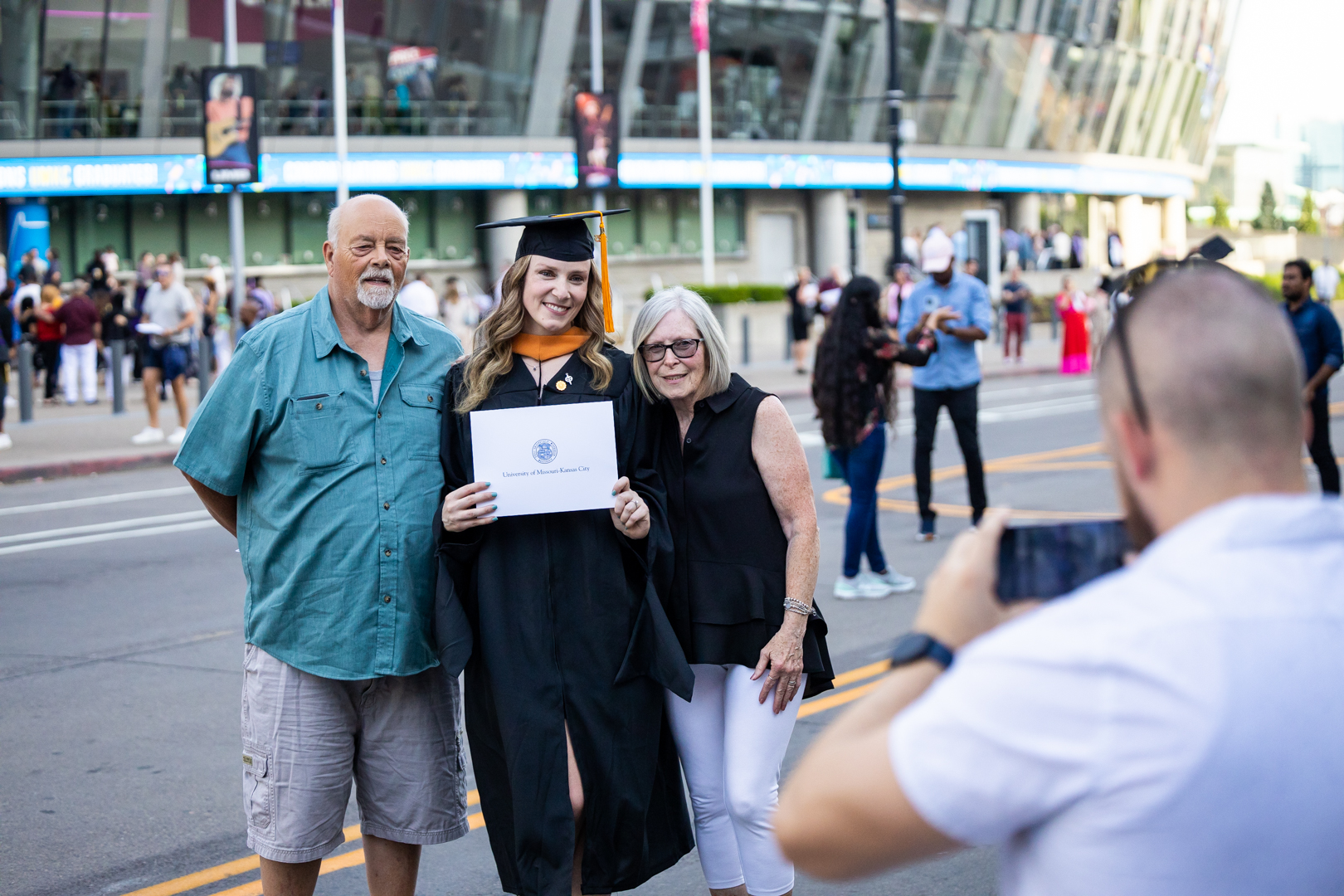 parents taking a photo with a student in cap and gown at commencement